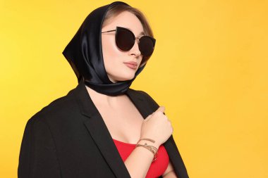 Dudak piercingli ve sarı arka planda güneş gözlüklü genç bir kadın. Metin için boşluk
