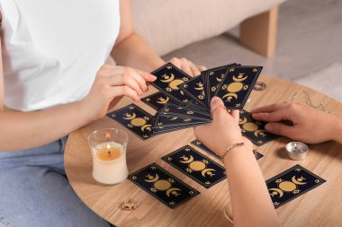 Bir kadın kapalı bir masada tarot kartı çekiyor, yakın plan. Falcı.