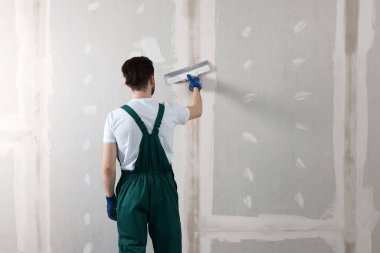 Üniformalı bir işçi, duvarda macun bıçağıyla duvarın arkasına bakıyor. Metin için boşluk