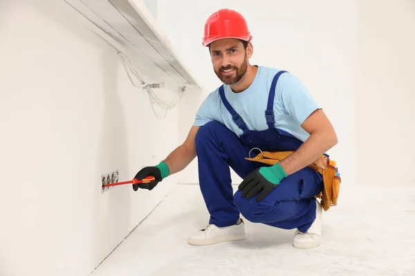 Electrician with screwdriver repairing power sockets indoors
