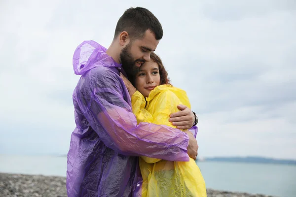 ビーチで雨の下で一緒に時間を楽しむレインコートの若いカップル — ストック写真