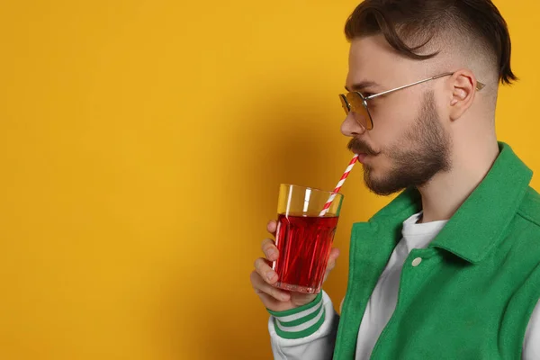 Handsome young man drinking juice on yellow background. Space for text