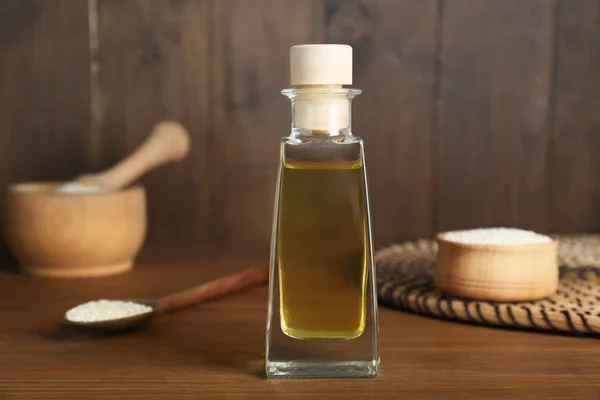 Fresh sesame oil in glass bottle and seeds on wooden table