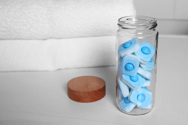 Glass jar with water softener tablets on washing machine in bathroom, space for text