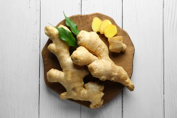 Fresh ginger with leaves on white wooden table, top view