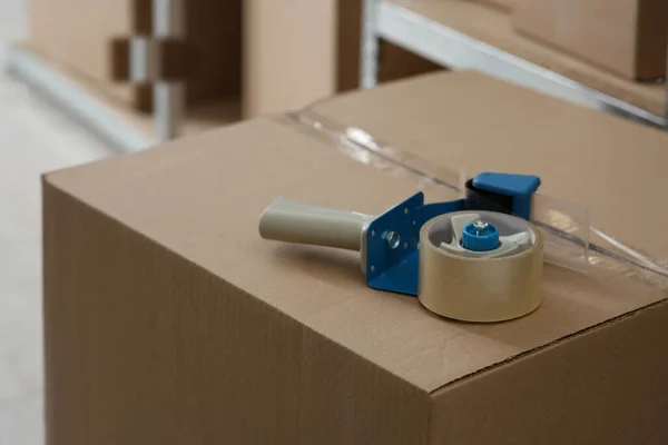 stock image Adhesive tape dispenser on cardboard box indoors