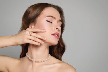 Gri arkaplanda zarif inci takılar takan genç bir kadın.