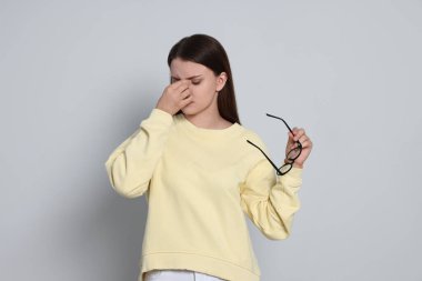 Young woman suffering from eyestrain on light background