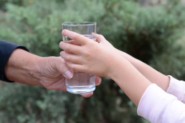 Çocuk dışarıdaki yaşlı kadına su veriyor, yakın plan.