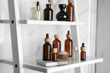 Temel yağlar, deniz tuzu ve diğer kozmetik ürünler banyodaki beyaz raf ünitesinde.