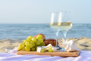 Beyaz şaraplı bardaklar ve kumlu deniz kıyısında piknik için atıştırmalıklar.