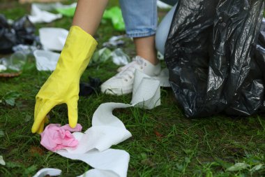Plastik çantalı bir kadın yeşil çimlerde çöp topluyor, yakın plan.