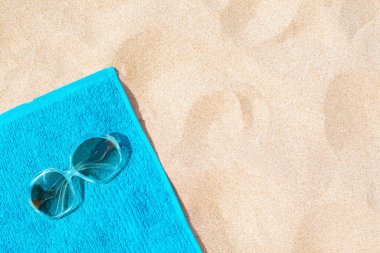 Soft blue beach towel with sunglasses on sand, top view. Space for text