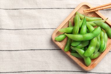 Kapsüllerde yeşil edamame fasulyesi ve havlunun üstünde yemek çubukları olan ahşap tabak, üst manzara. Metin için boşluk