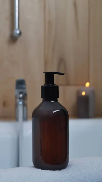 stock image Black bottle of bubble bath and candles on tub indoors