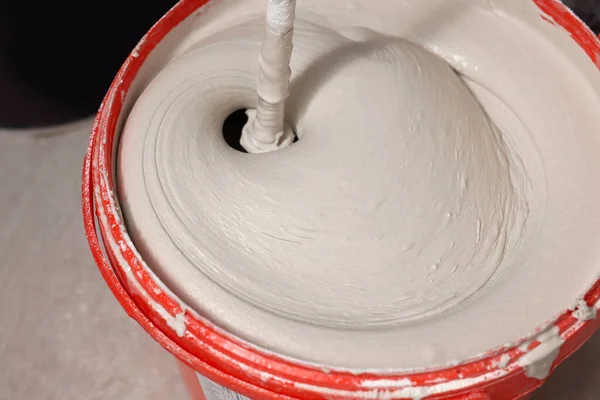 stock image Mixing putty with electric mixer in red bucket indoors, closeup