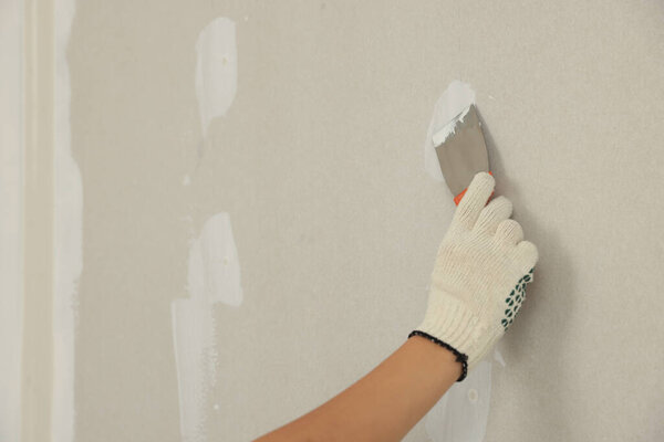 Worker plastering wall with putty knife, closeup. Space for text