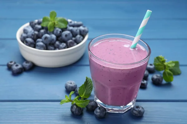Glass of blueberry smoothie with mint and fresh berries on blue wooden table. Space for text
