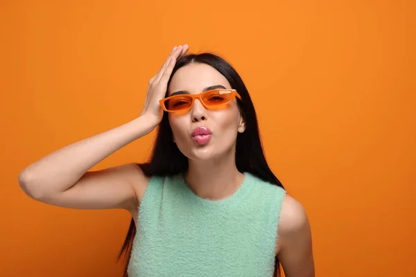 Piękna Młoda Kobieta Stylowych Okularach Przeciwsłonecznych Wieje Pocałunek Pomarańczowym Tle — Zdjęcie stockowe