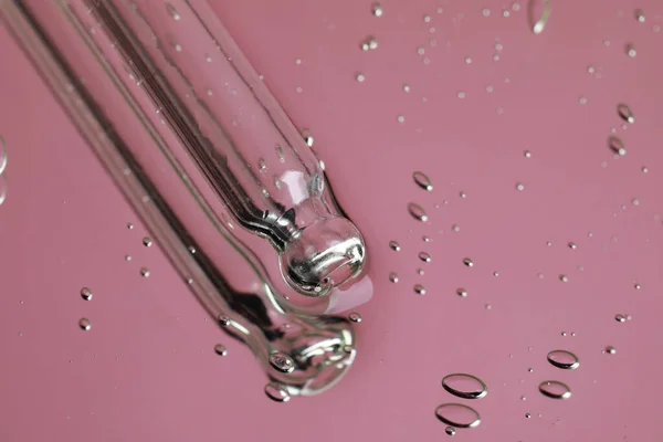 Pipette near serum drops on beautiful mirror, closeup with space for text. Toned in pink