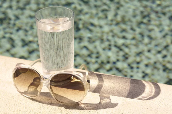 Stylowe Okulary Przeciwsłoneczne Szklanka Wody Pobliżu Odkrytego Basenu Słoneczny Dzień — Zdjęcie stockowe