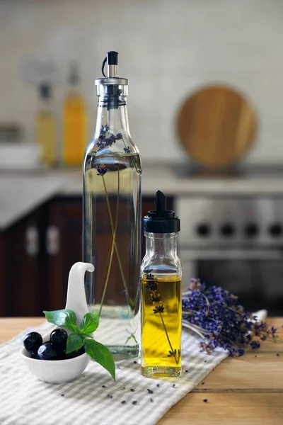 Different cooking oils, olives, basil and lavender flowers on wooden table in kitchen