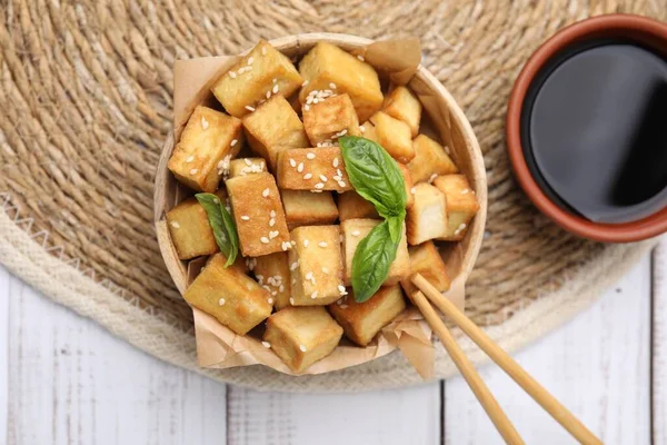 stock image Delicious fried tofu with basil and sesame seeds served on white wooden table, flat lay