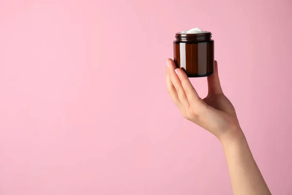 Woman with jar of face cream on pale pink background, closeup. Space for text