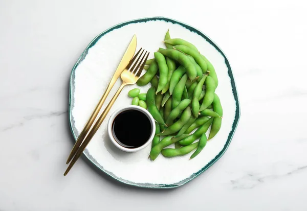 stock image Green edamame beans in pods served with soy sauce on white marble table, top view