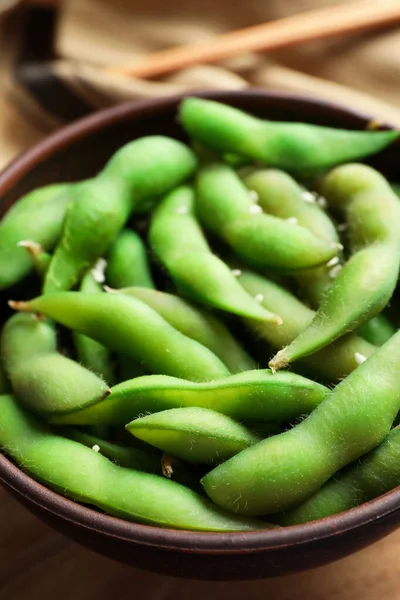 Bowl with green edamame beans in pods on table, closeup