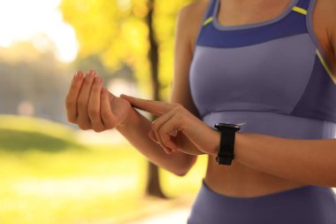 Woman checking pulse after training in park on sunny day. closeup clipart