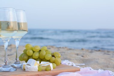 Beyaz şaraplı bardaklar ve kumlu sahilde atıştırmalıklar. Metin için boşluk