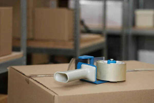 Adhesive tape dispenser on cardboard box indoors. Space for text