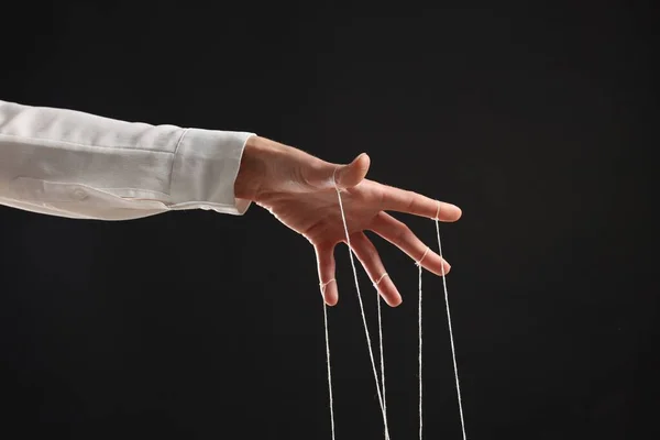 Woman pulling strings of puppet on black background, closeup