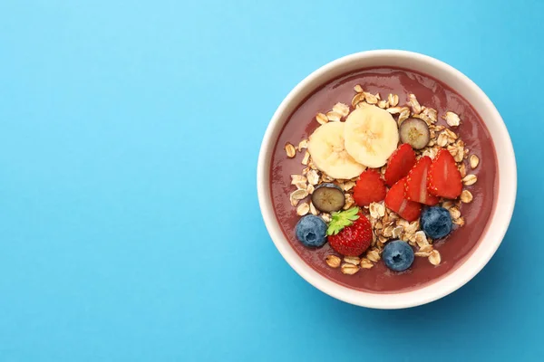 stock image Delicious smoothie bowl with fresh berries, banana and granola on light blue background, top view. Space for text