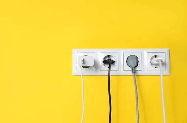 stock image Power sockets with inserted plugs on yellow wall, space for text. Electrical supply