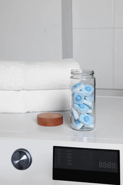 Glass jar with water softener tablets on washing machine in bathroom