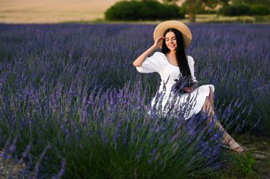 Beautiful young woman with bouquet sitting in lavender field