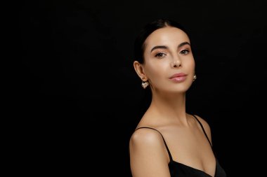 Siyah arka planda zarif inci küpeleri olan genç bir kadın.