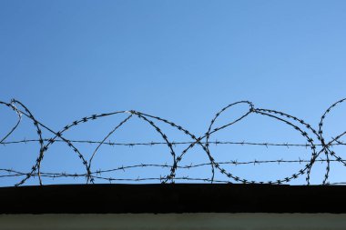 Açık mavi gökyüzünün altında metal dikenli tel