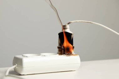 Gri duvara karşı beyaz masadaki güç bandında iltihaplı fişler. Elektrik kısa devresi