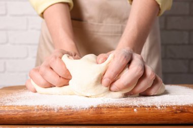 Beyaz tuğla duvarın yanındaki ahşap masada hamur yoğuran kadın, yakın plan.