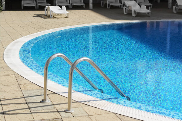 Outdoor swimming pool with ladder and handrails on sunny day