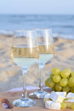 Beyaz şaraplı bardaklar ve kumlu deniz kıyısında piknik için atıştırmalıklar.