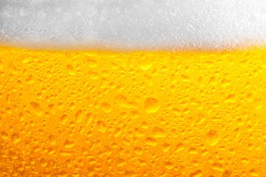 Glass of tasty cold beer with foam and condensation drops as background, closeup
