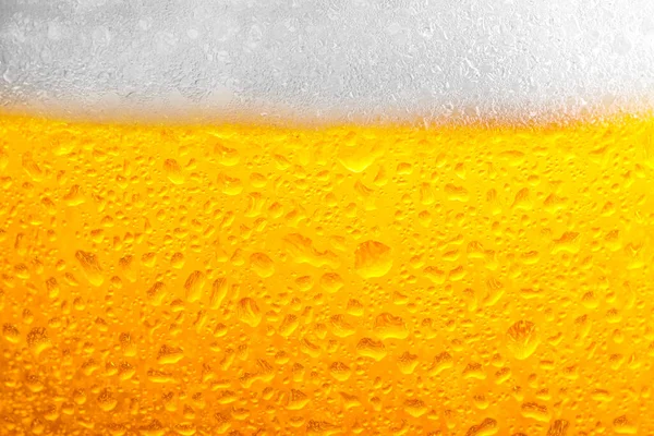 Glass of tasty cold beer with foam and condensation drops as background, closeup