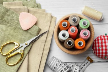 Beyaz ahşap masa üzerinde iplik makaraları ve dikiş araçları ile düz bileşim yatıyordu