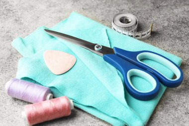 Gri arkaplanda makas, iplik makaraları ve dikiş araçları, yakın plan