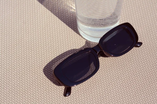 Snygga Solglasögon Och Glas Vatten Grå Yta Närbild — Stockfoto
