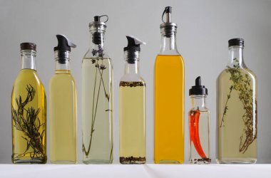 Bottles of different cooking oils on white wooden table against grey background